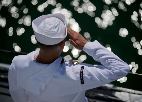 Navy sailor saluting while looking out into the ocean