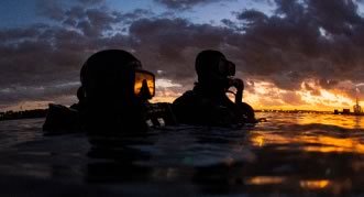 Two Navy crew on a ship looking out to the evening horizon
