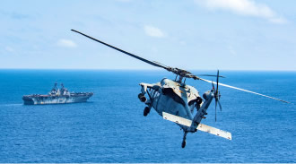 Decorative image of helicopter flying towards a naval ship in the ocean. 